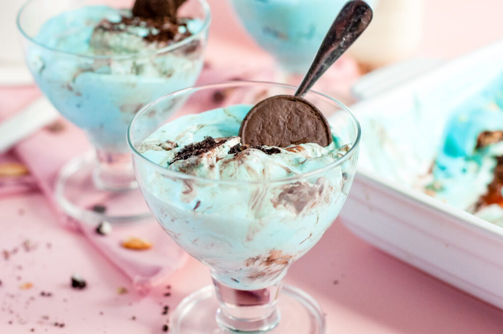 A square slice of Cookie Monster Icebox Dessert showing layers of Oreos, pudding, blue whipped topping, and Chips Ahoy cookies with sprinkles.