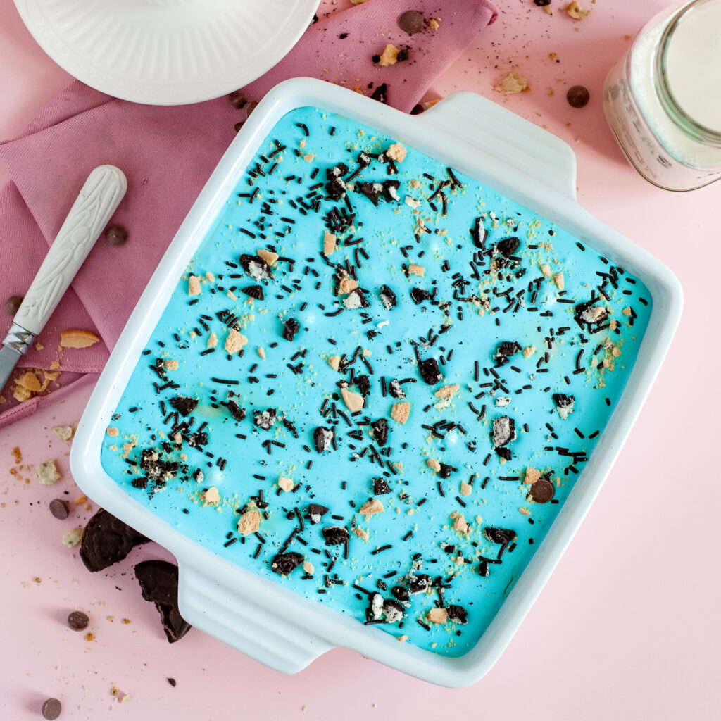 A square slice of Cookie Monster Icebox Dessert showing layers of Oreos, pudding, blue whipped topping, and Chips Ahoy cookies with sprinkles.