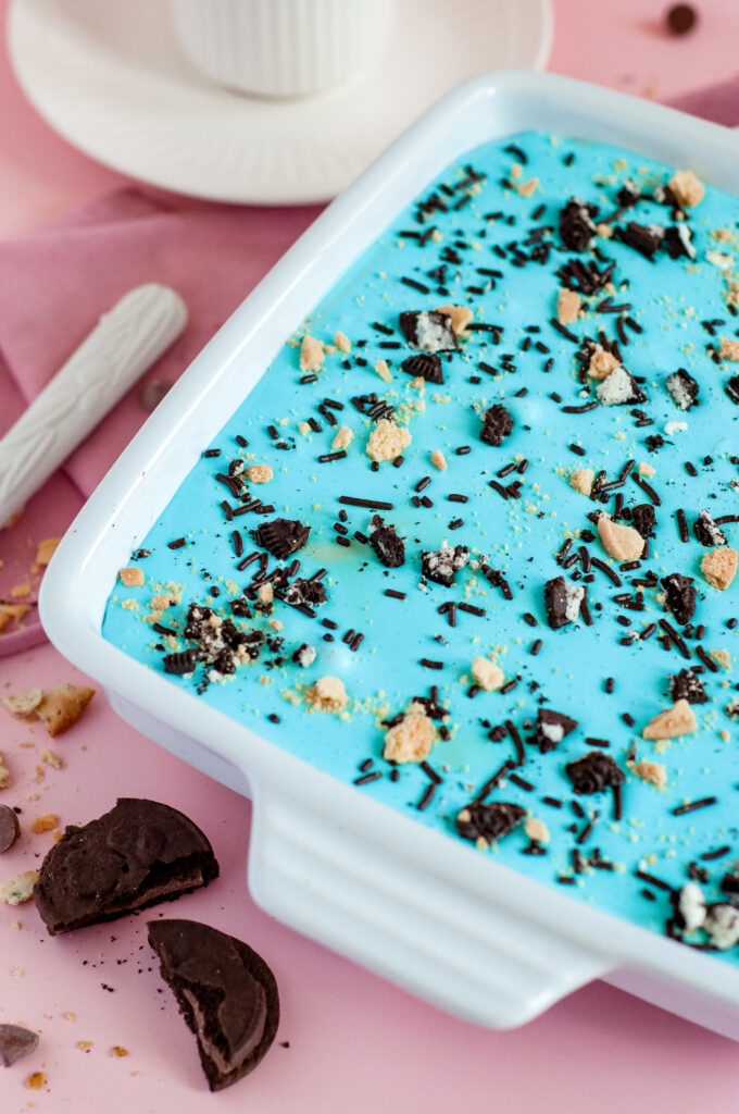 A square slice of Cookie Monster Icebox Dessert showing layers of Oreos, pudding, blue whipped topping, and Chips Ahoy cookies with sprinkles.