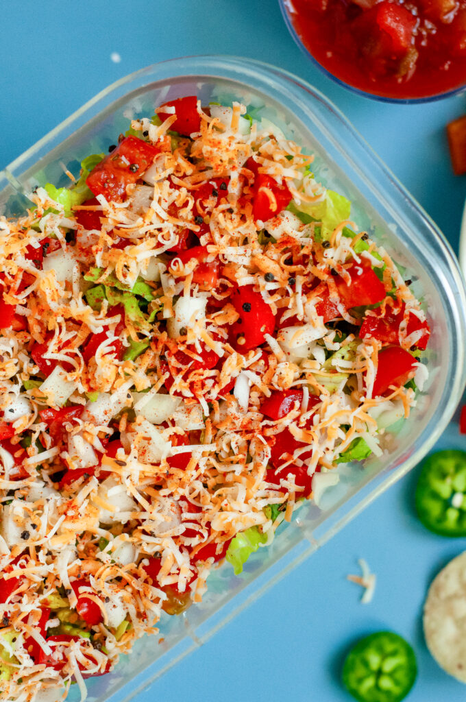 Creamy Jalapeño Taco Dip topped with cheese, tomatoes, onions, and seasoning in a clear dish.