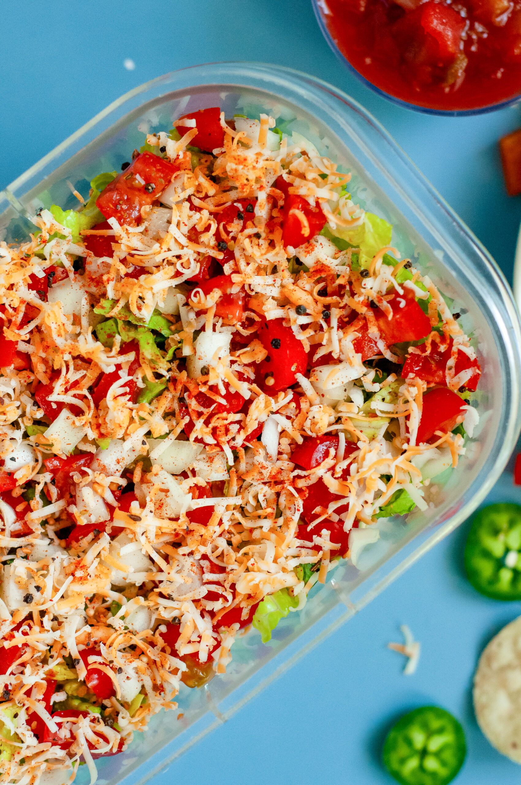 Creamy Jalapeño Taco Dip topped with cheese, tomatoes, onions, and seasoning in a clear dish.