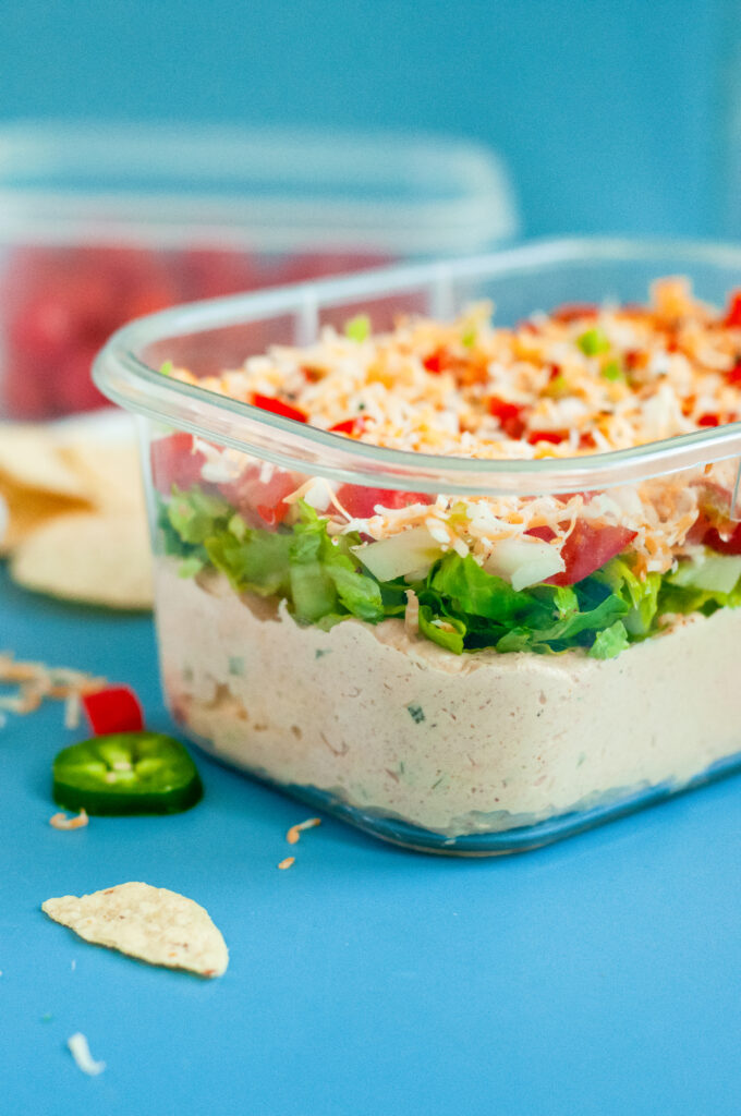 Creamy Jalapeño Taco Dip topped with cheese, tomatoes, onions, and seasoning in a clear dish.
