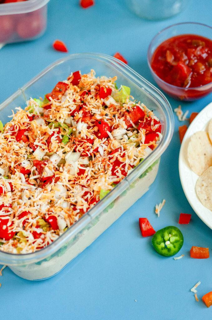 Creamy Jalapeño Taco Dip topped with cheese, tomatoes, onions, and seasoning in a clear dish.
