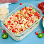 Creamy Jalapeño Taco Dip topped with cheese, tomatoes, onions, and seasoning in a clear dish.