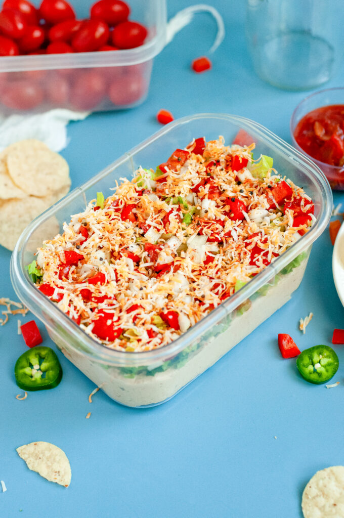Creamy Jalapeño Taco Dip topped with cheese, tomatoes, onions, and seasoning in a clear dish.