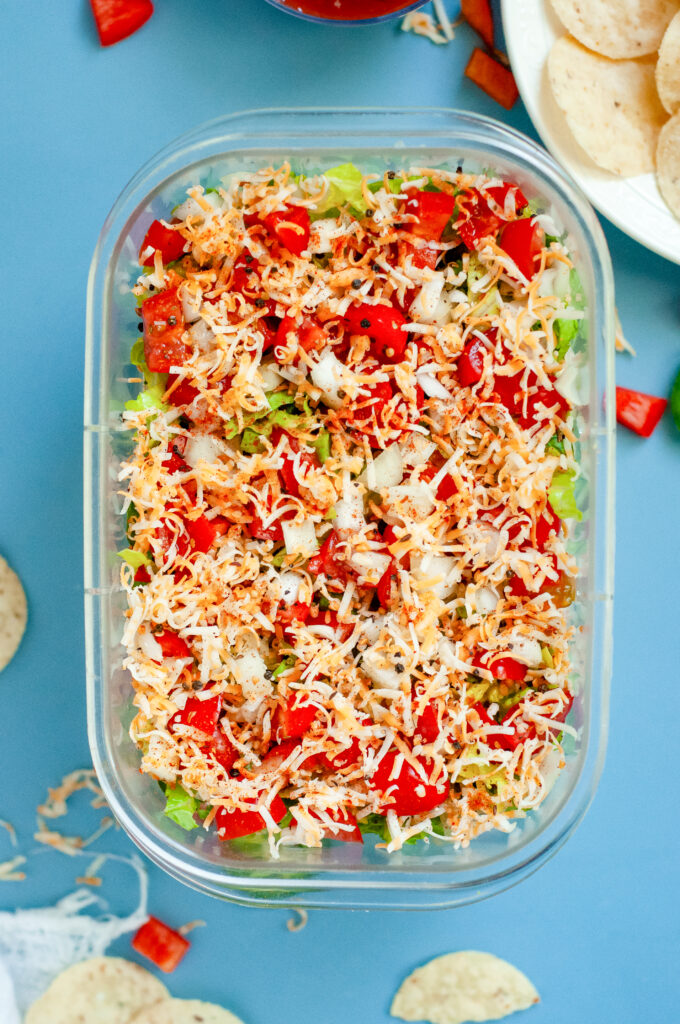 Creamy Jalapeño Taco Dip topped with cheese, tomatoes, onions, and seasoning in a clear dish.