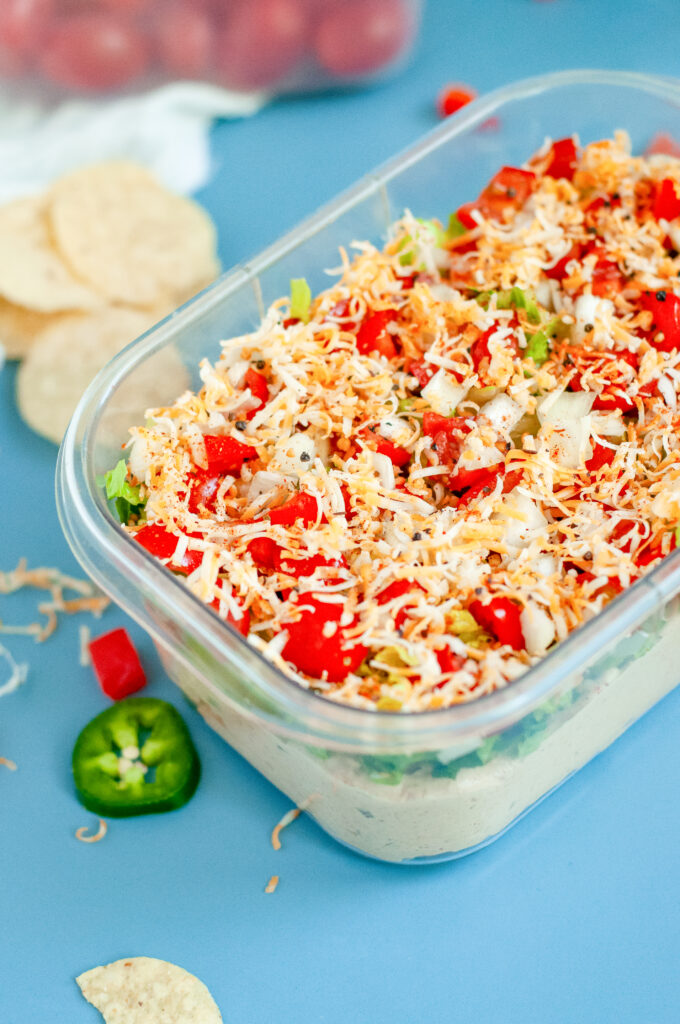 Creamy Jalapeño Taco Dip topped with cheese, tomatoes, onions, and seasoning in a clear dish.