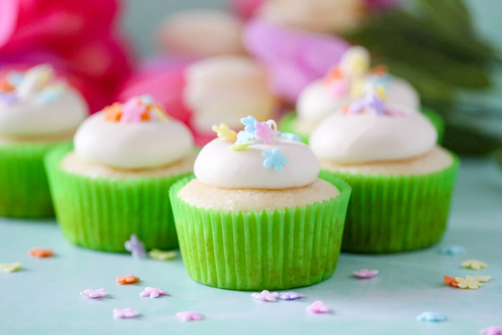 Almond cupcakes topped with honey cream cheese frosting, spring sprinkles, and a drizzle of golden honey on a white plate.