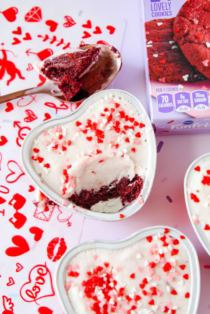 Heart-shaped red velvet cookie cups filled with ice cream, topped with colorful sprinkles, served in mini containers—perfect for a festive family treat.