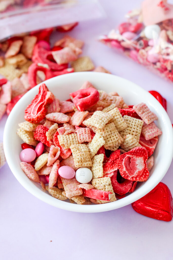 Bowl of Strawberry Chex Snack Mix with pink and red M&Ms, white chocolate pretzels, and freeze-dried strawberries – a festive, crunchy snack.