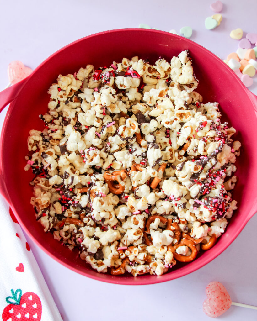 A bowl of Valentine’s Loaded Kettlecorn with chocolate drizzle, pretzels, and festive pink and red sprinkles, perfect for a sweet-and-salty holiday treat.