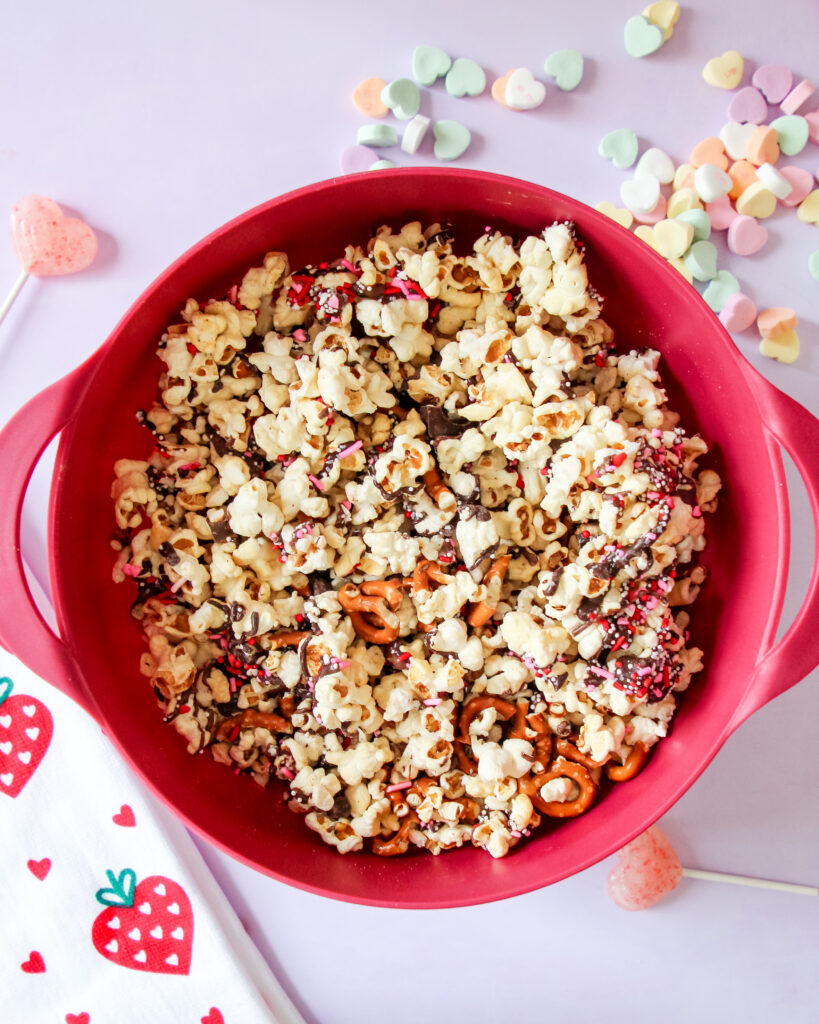 A bowl of Valentine’s Loaded Kettlecorn with chocolate drizzle, pretzels, and festive pink and red sprinkles, perfect for a sweet-and-salty holiday treat.