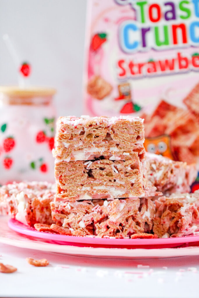 A batch of Strawberry Toast Crunch  Bars, drizzled with pink chocolate and topped with freeze-dried strawberry pieces, cut into squares.
