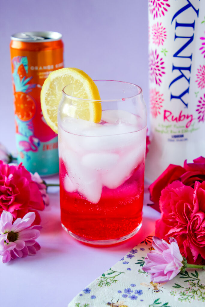 A vibrant cocktail in a tall glass, featuring vodka, grenadine, and Orange, garnished with a fresh lemon slice.