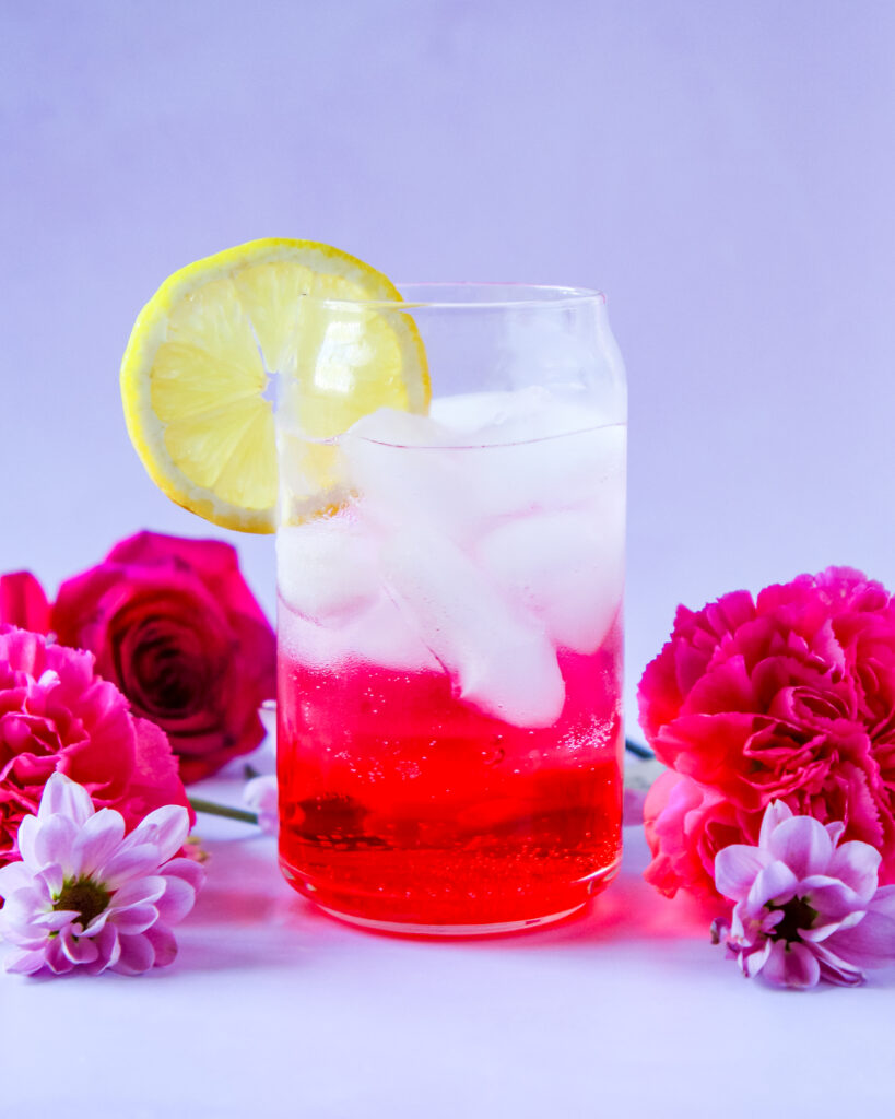 A vibrant cocktail in a tall glass, featuring vodka, grenadine, and Orange, garnished with a fresh lemon slice.