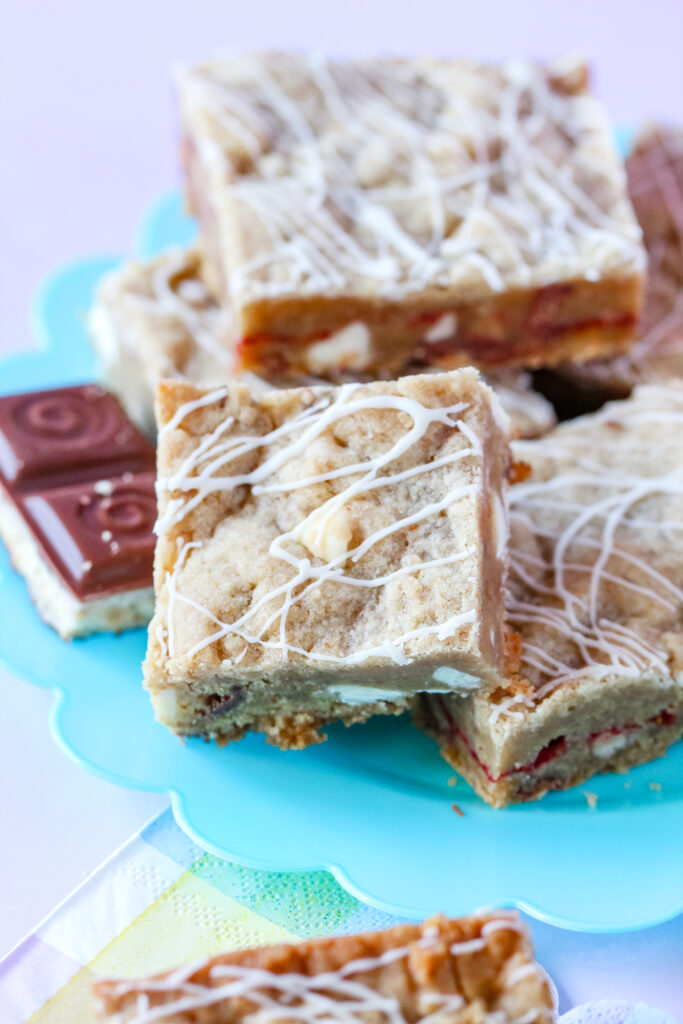 A batch of golden-brown Strawberry Candy Bar Blondies with a drizzle of white chocolate, featuring a soft center and bursts of strawberry and candy bar pieces.