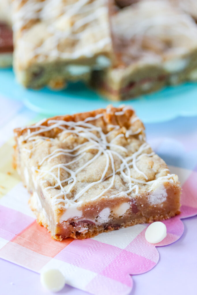 A batch of golden-brown Strawberry Candy Bar Blondies with a drizzle of white chocolate, featuring a soft center and bursts of strawberry and candy bar pieces.