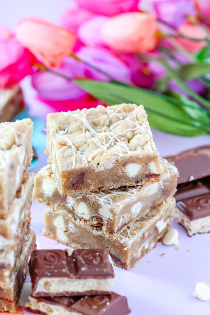 A batch of golden-brown Strawberry Candy Bar Blondies with a drizzle of white chocolate, featuring a soft center and bursts of strawberry and candy bar pieces.