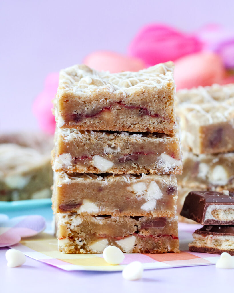 A batch of golden-brown Strawberry Candy Bar Blondies with a drizzle of white chocolate, featuring a soft center and bursts of strawberry and candy bar pieces.