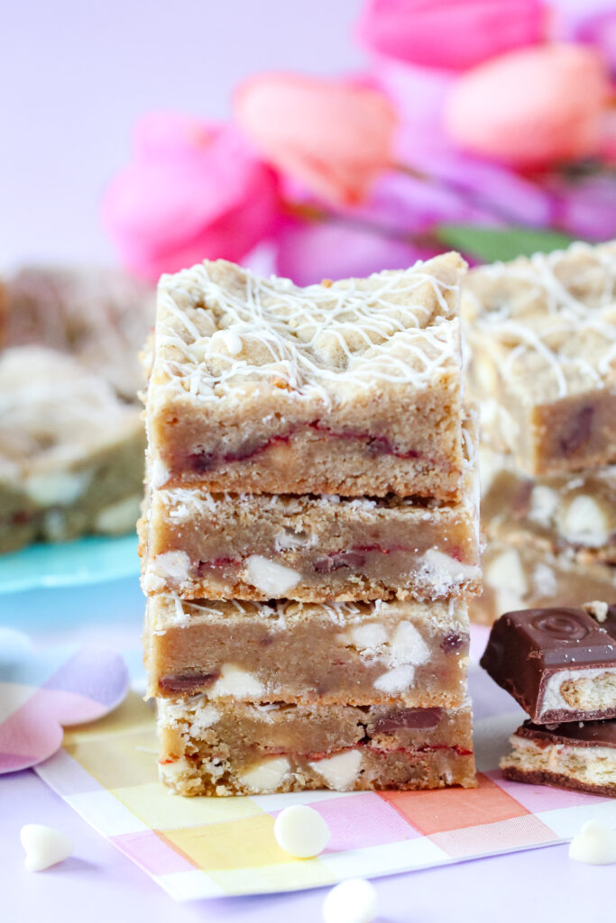 A batch of golden-brown Strawberry Candy Bar Blondies with a drizzle of white chocolate, featuring a soft center and bursts of strawberry and candy bar pieces.