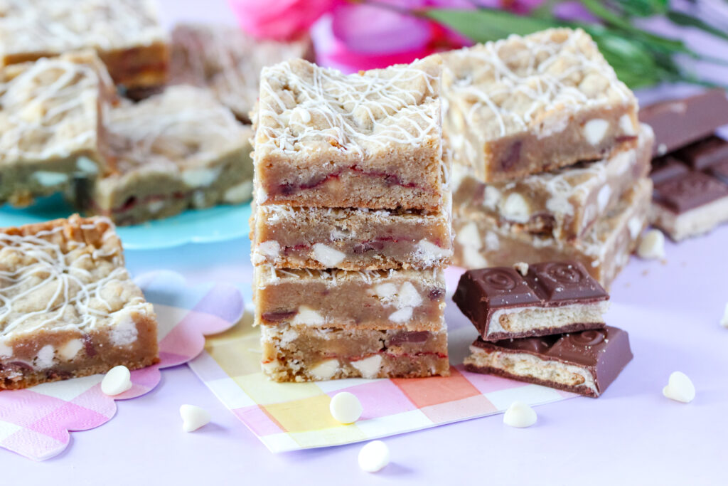 A batch of golden-brown Strawberry Candy Bar Blondies with a drizzle of white chocolate, featuring a soft center and bursts of strawberry and candy bar pieces.