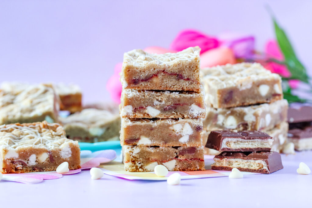 A batch of golden-brown Strawberry Candy Bar Blondies with a drizzle of white chocolate, featuring a soft center and bursts of strawberry and candy bar pieces.