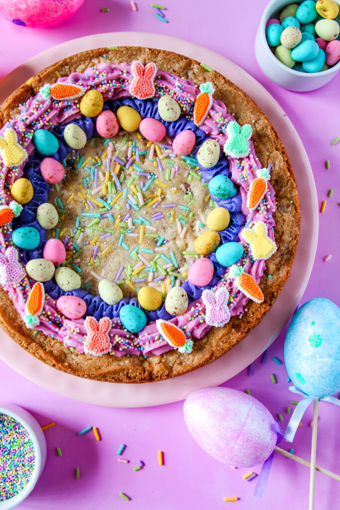 Egg-stravaganza Cookie Cake – a golden chocolate chip cookie cake packed with Easter candies, topped with pastel buttercream swirls and festive sprinkles.