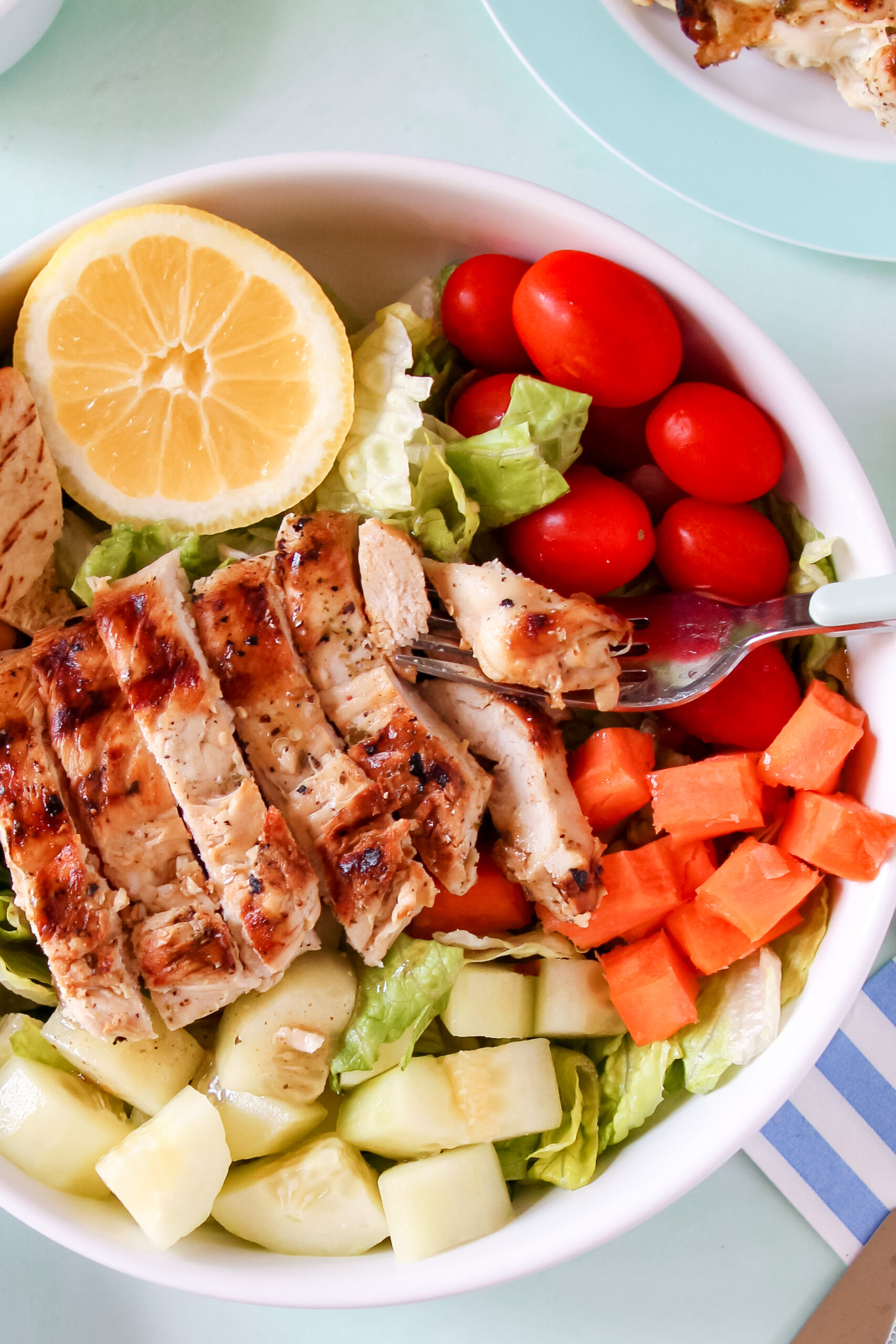 Grilled lemon garlic chicken on a plate with fresh herbs, a side of rice, and a lemon wedge, served outdoors on a sunny day.