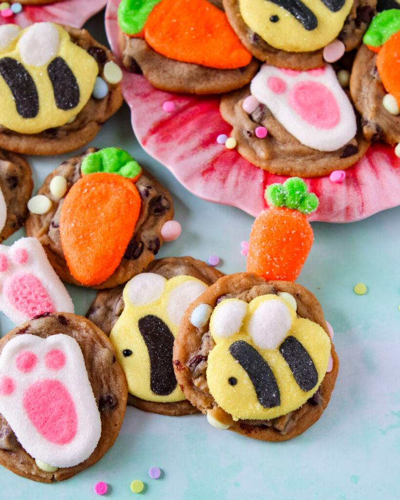 Cookies lined up on a parchment-lined baking sheet, each featuring a different marshmallow shape like flowers, bunnies, and bees.
