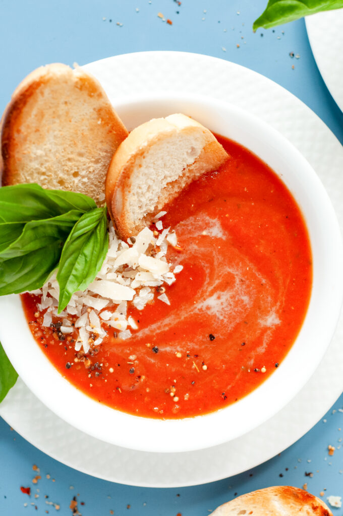 A bowl of creamy tomato basil soup topped with grated Parmesan and fresh basil, served with grilled bread.