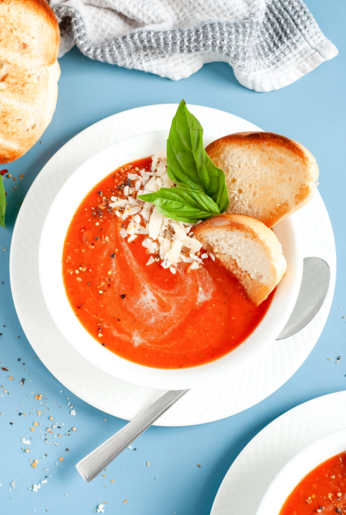 A bowl of creamy tomato basil soup topped with grated Parmesan and fresh basil, served with grilled bread.