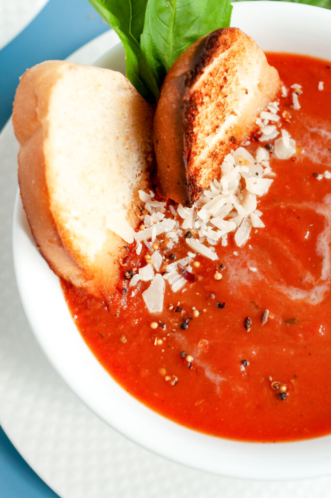 A bowl of creamy tomato basil soup topped with grated Parmesan and fresh basil, served with grilled bread.