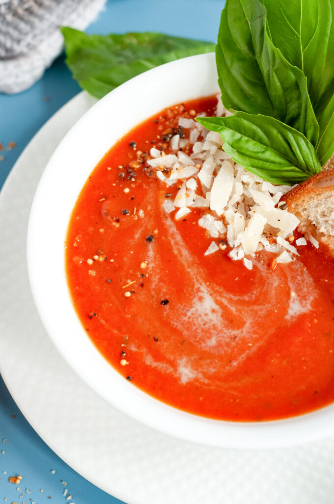 A bowl of creamy tomato basil soup topped with grated Parmesan and fresh basil, served with grilled bread.