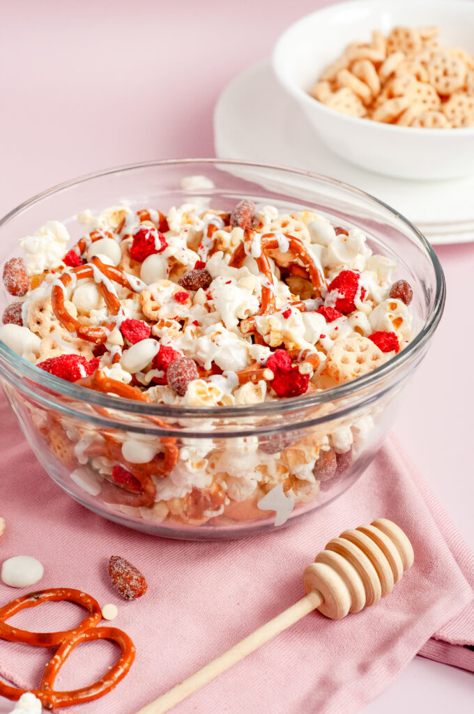 A bowl of honey bee snack mix with popcorn, pretzels, yogurt raisins, almonds, and white chocolate drizzle