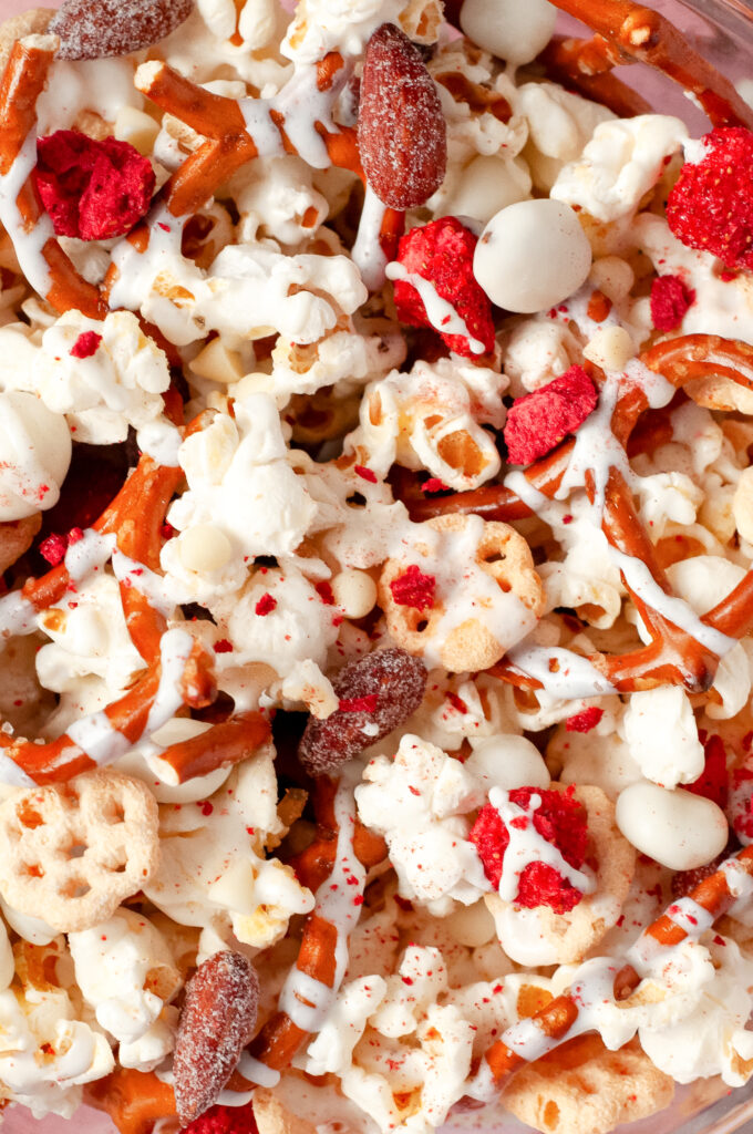 A bowl of honey bee snack mix with popcorn, pretzels, yogurt raisins, almonds, and white chocolate drizzle