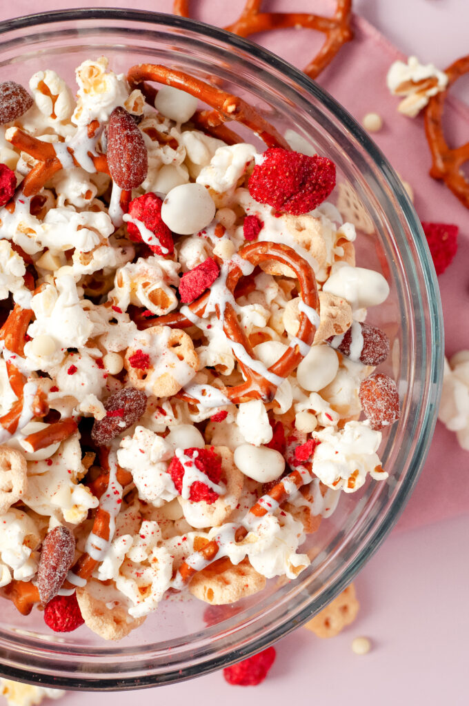 A bowl of honey bee snack mix with popcorn, pretzels, yogurt raisins, almonds, and white chocolate drizzle