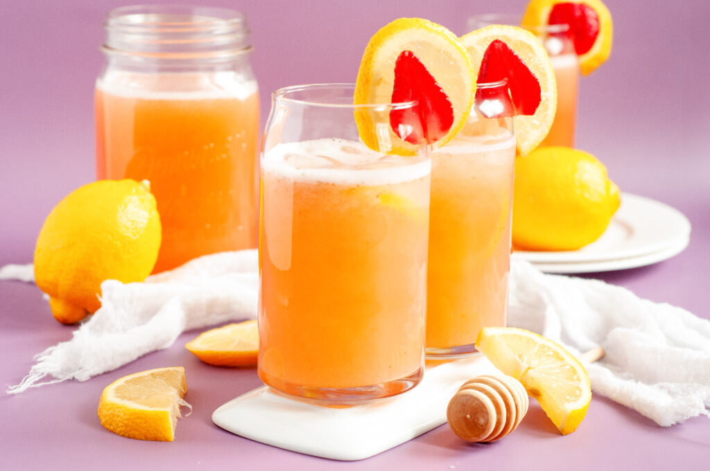 A glass pitcher of fresh strawberry lemonade with floating lemon slices and mint leaves, served over ice with fresh strawberries on the side.