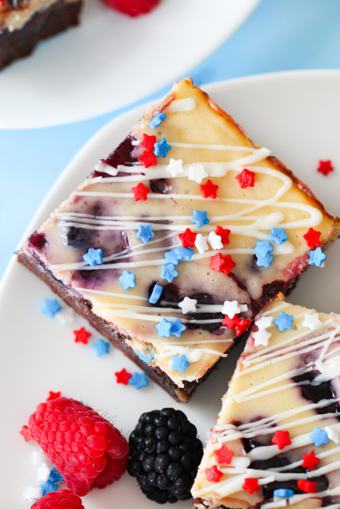 Patriotic cheesecake brownies with red and blue jam swirls, white chocolate drizzle, and star-shaped sprinkles on top.