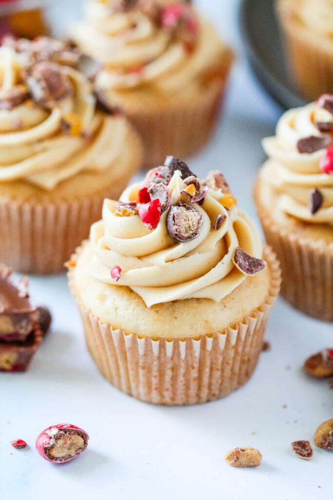 Strawberry PB&J cupcakes topped with fluffy peanut butter frosting, chopped Reese’s PB&J Cups, and colorful candy pieces.