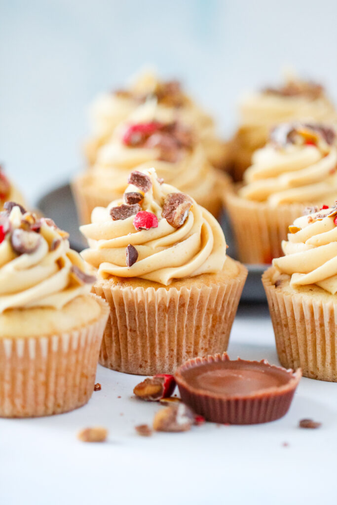 Strawberry PB&J cupcakes topped with fluffy peanut butter frosting, chopped Reese’s PB&J Cups, and colorful candy pieces.