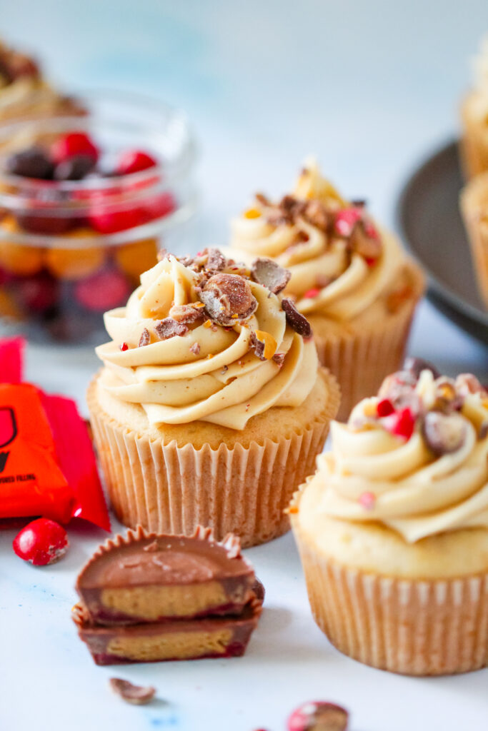 Strawberry PB&J cupcakes topped with fluffy peanut butter frosting, chopped Reese’s PB&J Cups, and colorful candy pieces.
