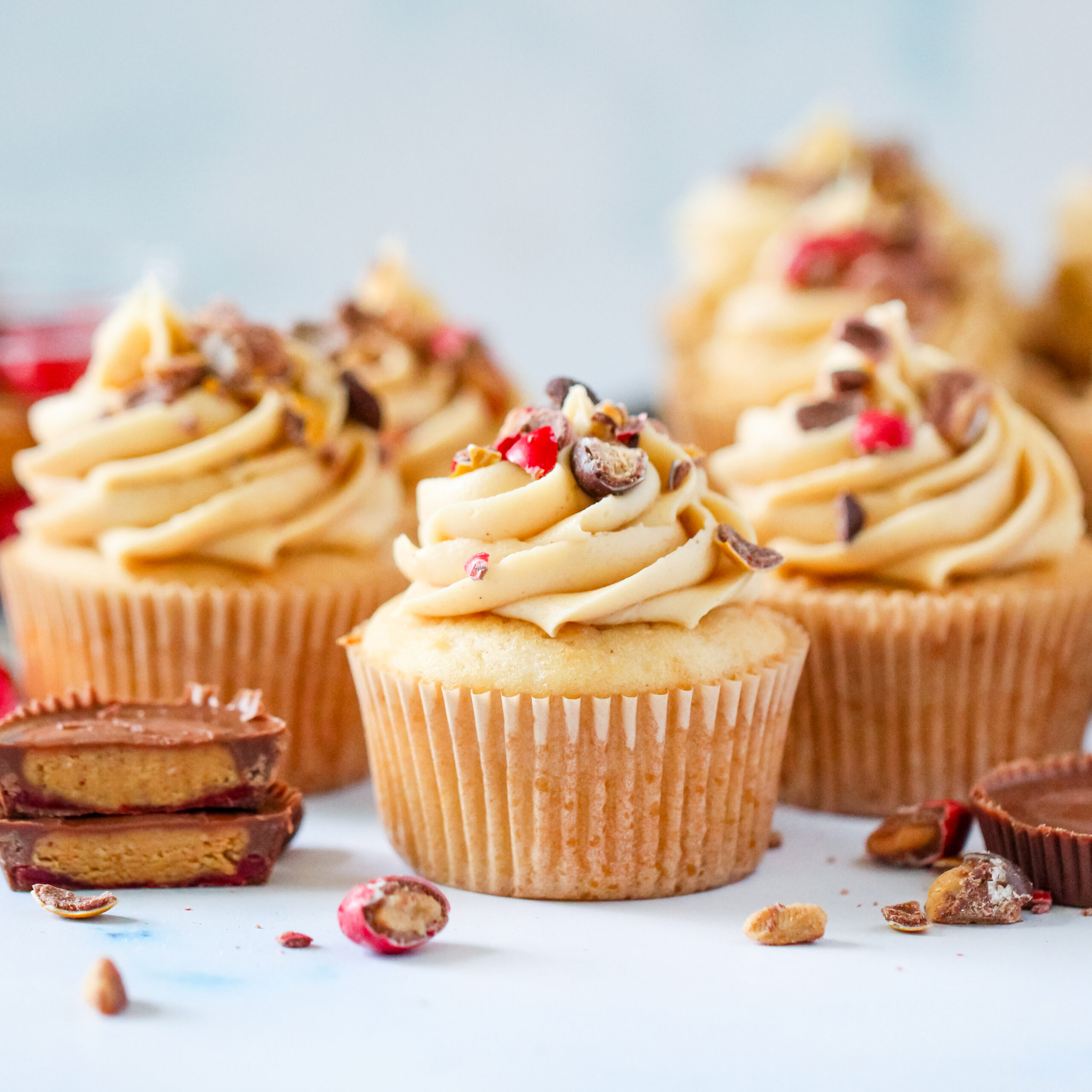 Strawberry PB&J cupcakes topped with fluffy peanut butter frosting, chopped Reese’s PB&J Cups, and colorful candy pieces.