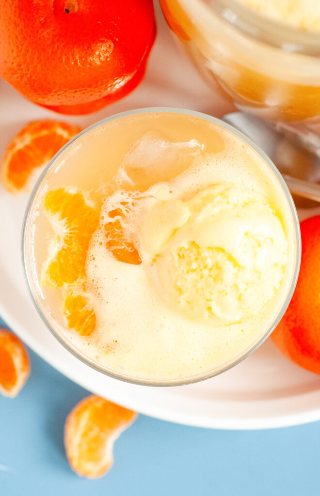 A punch bowl filled with orange sherbet punch, garnished with orange slices and cherries, surrounded by bright summer party decor.
