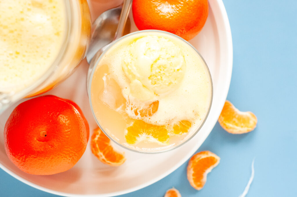 A punch bowl filled with orange sherbet punch, garnished with orange slices and cherries, surrounded by bright summer party decor.