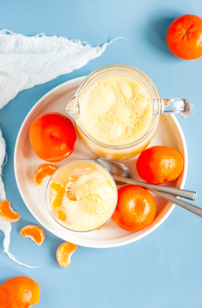 A punch bowl filled with orange sherbet punch, garnished with orange slices and cherries, surrounded by bright summer party decor.