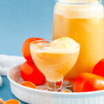 A punch bowl filled with orange sherbet punch, garnished with orange slices and cherries, surrounded by bright summer party decor.