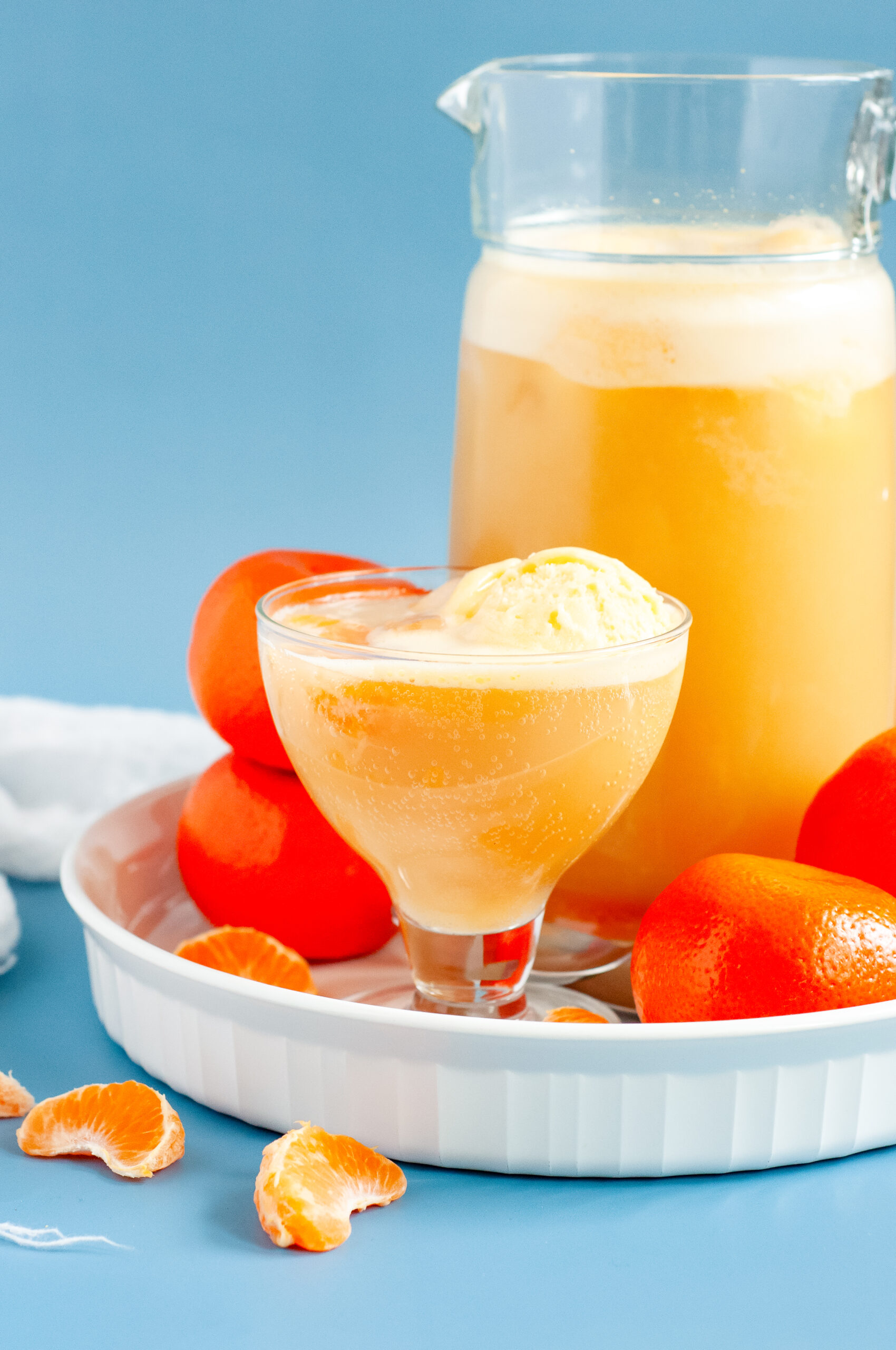 A punch bowl filled with orange sherbet punch, garnished with orange slices and cherries, surrounded by bright summer party decor.
