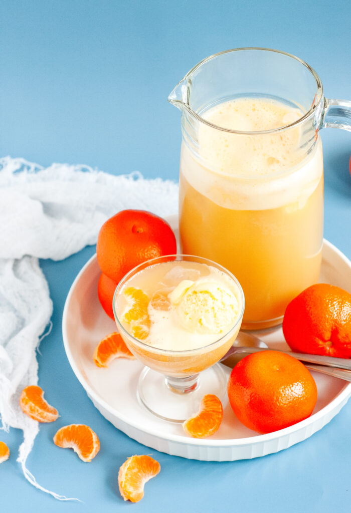 A punch bowl filled with orange sherbet punch, garnished with orange slices and cherries, surrounded by bright summer party decor.