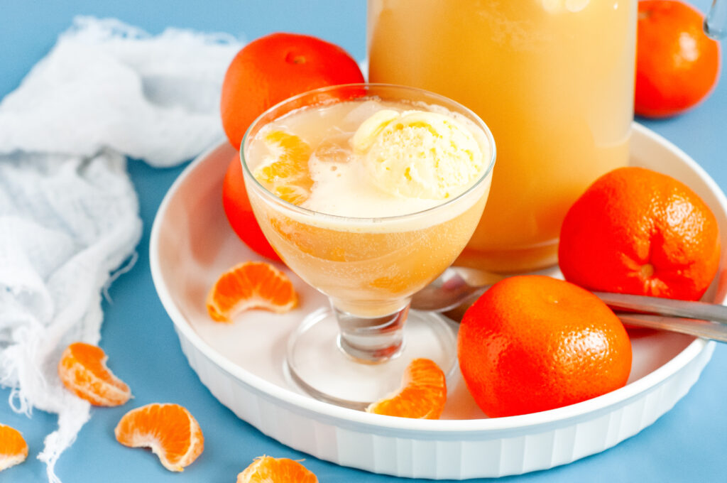 A punch bowl filled with orange sherbet punch, garnished with orange slices and cherries, surrounded by bright summer party decor.