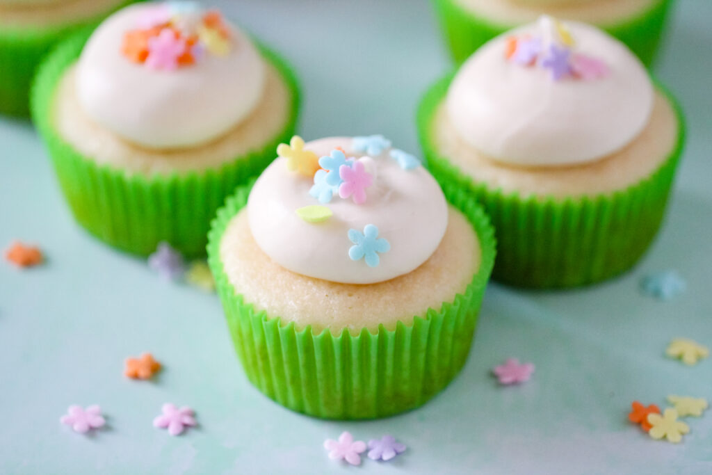 Almond cupcakes topped with honey cream cheese frosting, spring sprinkles, and a drizzle of golden honey on a white plate.